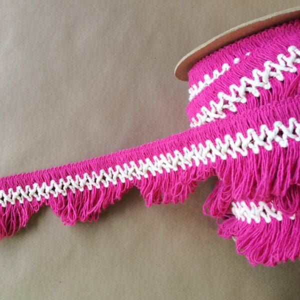 A pink and white scalloped lace fringe on top of a spool.