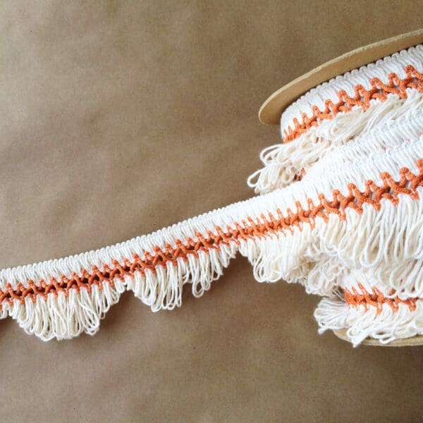 A white and orange scalloped lace fringe on a brown surface.