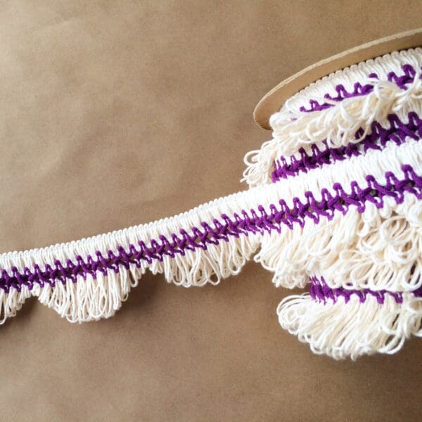 A white and purple Scalloped Lace Fringe on a brown surface.