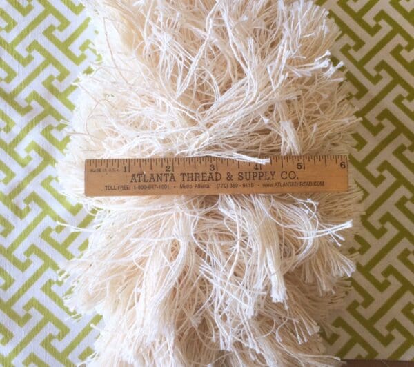 A roll of 4.5IN Extra Thick Textured Brush Fringe-Natural Cotton with a ruler on it.