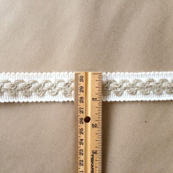A Barnsley 1.5 Gimp-Natural Cotton and Linen is used to measure the length of a braided ribbon.