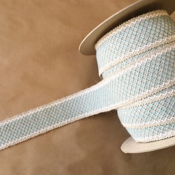 A blue and white Camlet and Camlet Wool 2.25 spool of ribbon on a table.