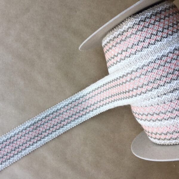 A pink and grey striped Camlet and Camlet Wool 2.25 ribbon on top of a table.