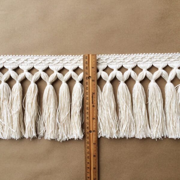 A Diamond Double Knot Fringe 6.5IN-Natural Cotton measuring tape with tassels on it.