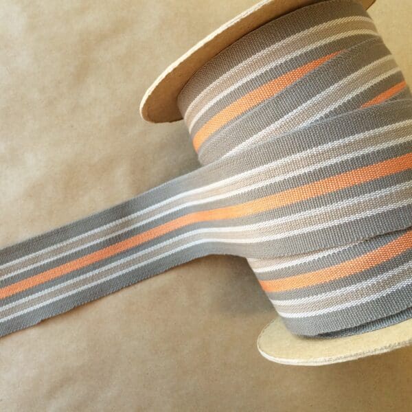 A grey and orange striped Eden 2 1/4 ribbon on a spool.