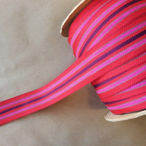 A red and purple striped ribbon on top of an Eden 1.5 and 2IN Tapes-Indoor and Outdoor spool.