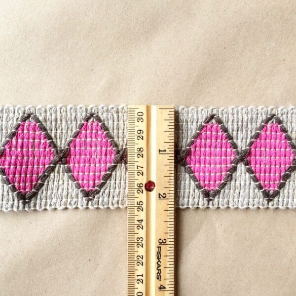 A pink and grey woven belt with a Harlequin 2IN Tape.