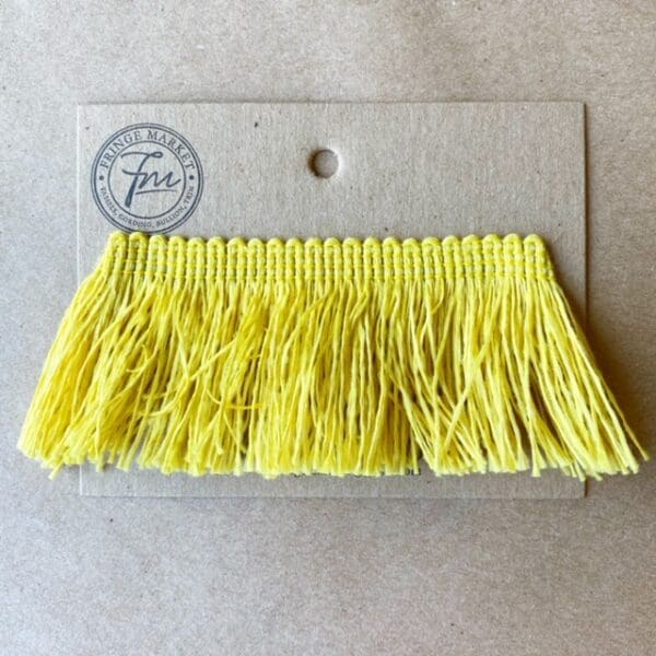 A yellow Outdoor 2IN Cut Brush Fringe trim on a piece of paper.