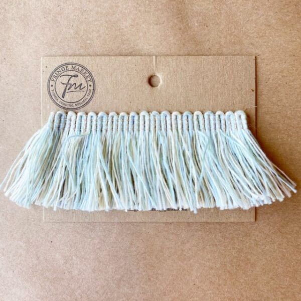 A white and blue Outdoor 2IN Cut Brush Fringe trim on a piece of paper.