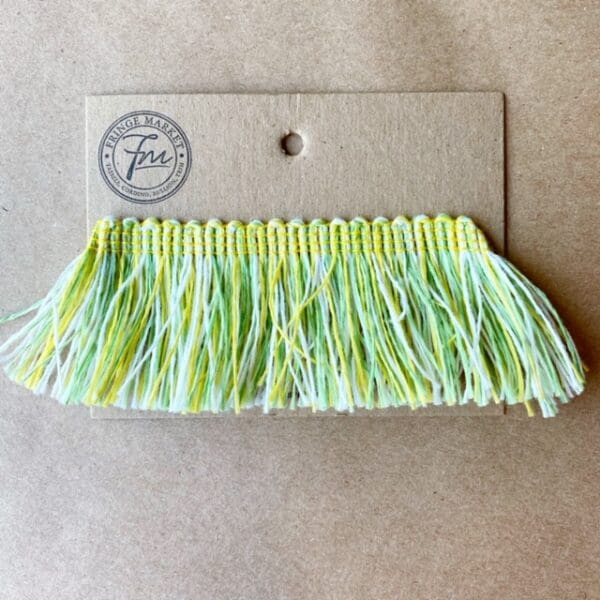A green and yellow Outdoor 2IN Cut Brush Fringe trim on a piece of paper.