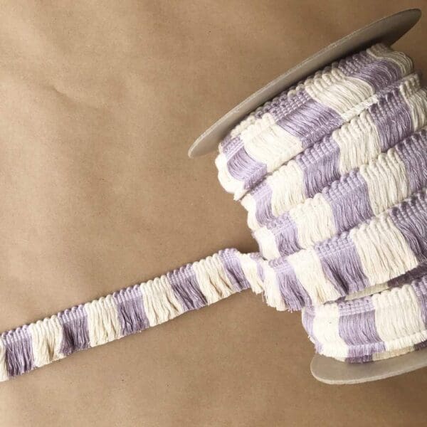 A purple and white striped 1.5 Big Top Cut Fringe ribbon on a spool.