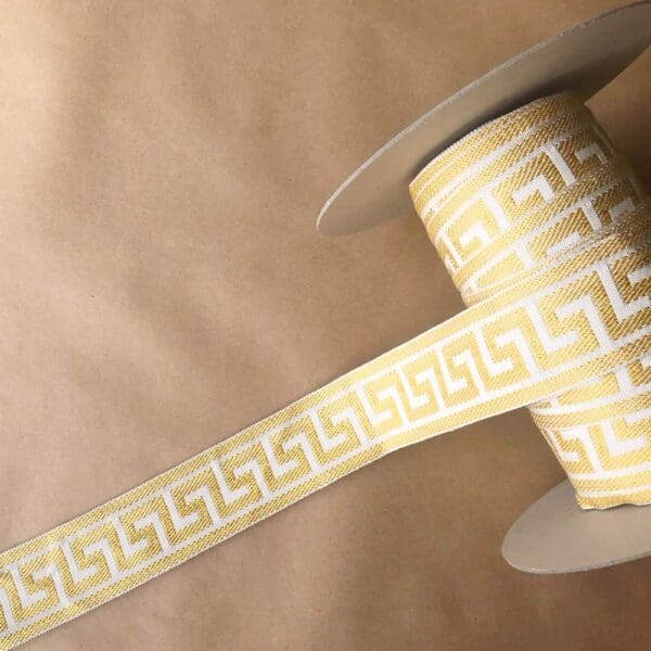 A yellow and white spool of Greek Key, Silk 2 1/4 IN ribbon with a greek design on it.