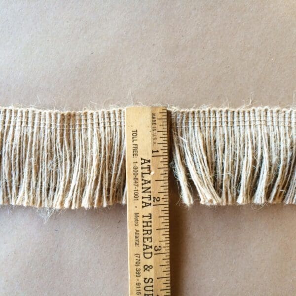 A measuring tape with a Jute 2IN Brush Fringe next to it.