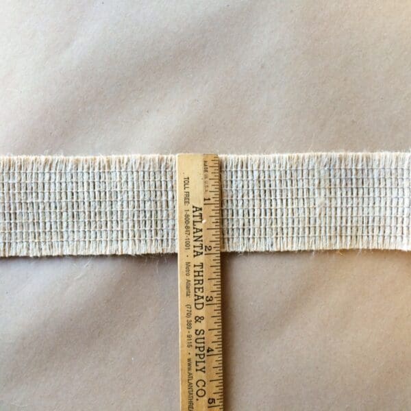 A Jute 2IN Double Edge Cut Tape is being used to measure the length of a piece of fabric.