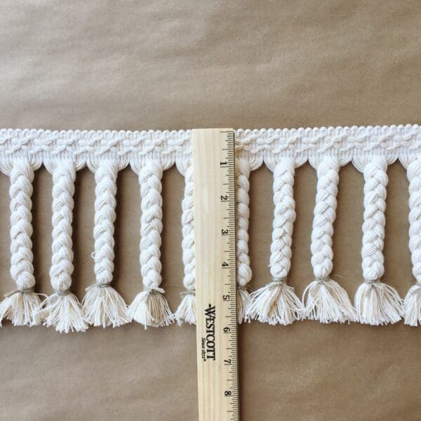 A measuring tape with Moroccan Braided Fringe 6IN on it.