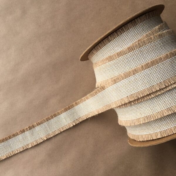 A spool of Navajo Jute Tapes 2IN ribbon on a brown surface.