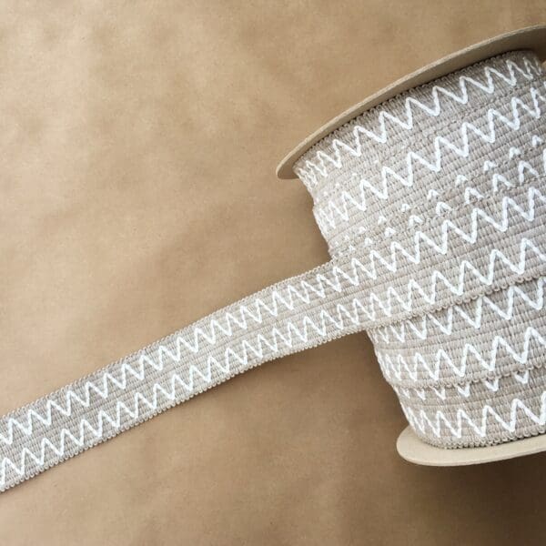 A spool of Essex Outdoor Tapes 2IN beige and white zigzag ribbon.