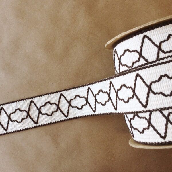 A white and brown ribbon with a pattern on it called Quincy Tapes.