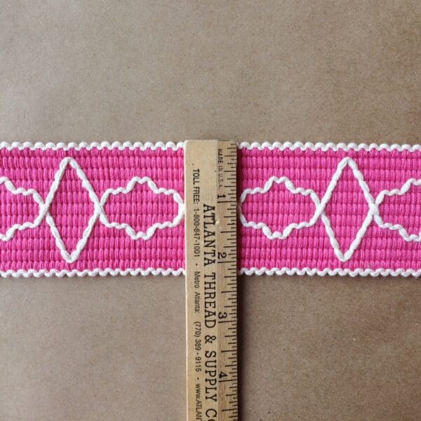 A pink and white embroidered Quincy Tapes on a ruler.