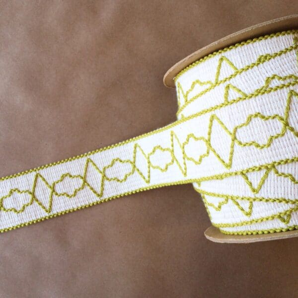 A roll of Quincy Tapes yellow and white embroidered ribbon.