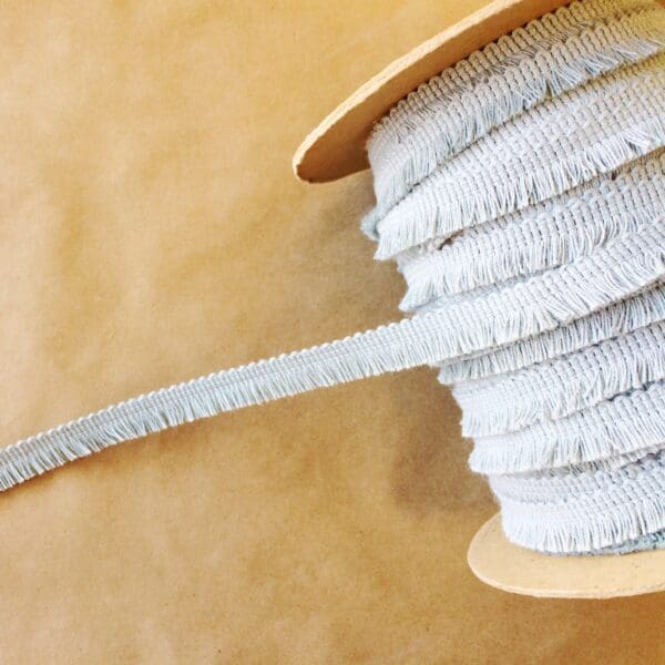 A spool of white ribbon with Sef-Selvedge Edge Fringe on it.
