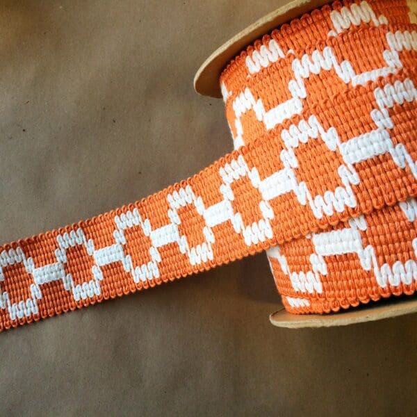 An orange and white Soho 2 1/4 woven ribbon on a table.