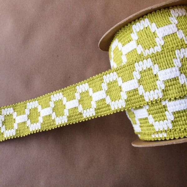 A green and white woven ribbon on a Soho 2 1/4 surface.