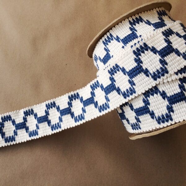 A blue and white Soho 2 1/4 woven ribbon on a brown surface.