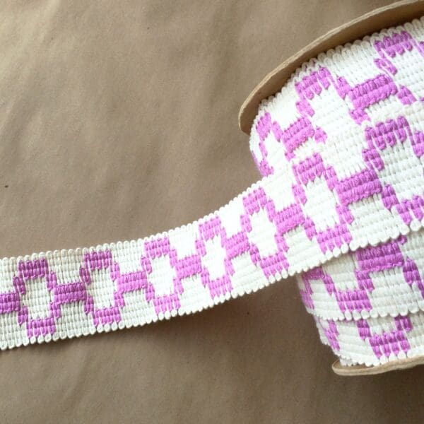 A pink and white Soho 2 1/4 woven ribbon on a table.