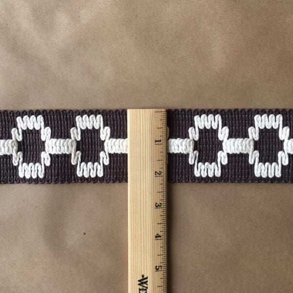 A brown and white woven Soho 2 1/4 belt with a ruler.