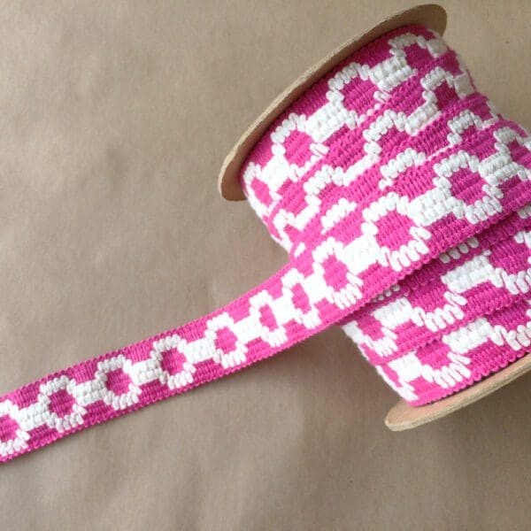 A pink and white Soho 1.5 crocheted ribbon on a spool.