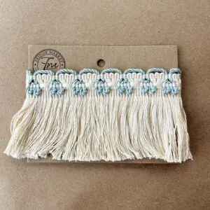 A card displaying a row of pastel blue and white Greenwich Silk Skirt Fringe tassels against a beige background.