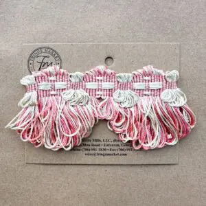 Windsor Scalloped Fringe displaying multiple tassels in pink, white, and red hanging from loops, against a cardboard background with a company logo and contact information.